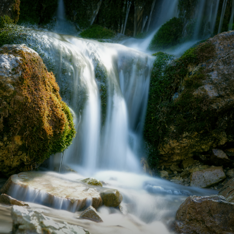 Langzeitbelichtung eines kleinen Wasserfalls zwischen moosbewachsenen Felsen.